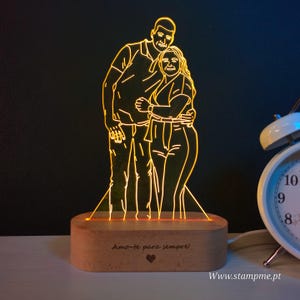 Pode incluir: Uma luz noturna LED personalizada com uma base de madeira. A luz apresenta um contorno de um casal abraçando-se. A base tem o texto "Amo-te para sempre!" e um coração.