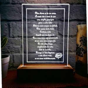 Peut inclure: Une enseigne lumineuse blanche avec une base en bois affiche un poème en portugais. Le poème se lit comme suit : "Não chores se tu me amas. A morte não é mais do que uma simples passagem para o outro lado. Fala-me como sempre me falaste, Não quers ser-te triste. Continua rindo daquilo que nos fazia rir. Que o meu nome seja pronunciado cá em casa, como sempre foi. Eu não estou longe, simplesmente do outro lado do caminho. Enauga as tuas lágrimas e não chores mais, se me amas verdadeiramente."