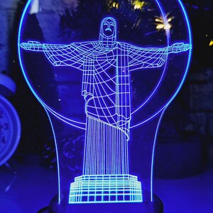 Może przedstawiać: Niebieska, trójwymiarowa, drukowana lampa w kształcie pomnika Chrystusa Odkupiciela w Rio de Janeiro w Brazylii. Lampa jest podświetlana od wewnątrz, tworząc efekt świecenia.