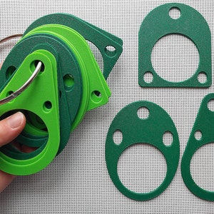 May include: A set of green and light green gasket shapes, including circles, ovals, and triangles, with holes in them. The gaskets are arranged in a pile and held in a hand.