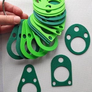 May include: A set of green and light green rubber gaskets of various sizes and shapes, including round, oval, and teardrop shapes. The gaskets are arranged in a fan shape and held together by a metal ring.