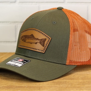 May include: A green and orange trucker hat with a brown leather patch featuring a trout design. The hat has a mesh back and a curved brim.
