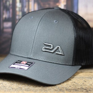 May include: Gray and black baseball cap with a curved brim and a mesh back. The cap features an embroidered logo on the front and a tag on the side. The hat is made of a durable material.