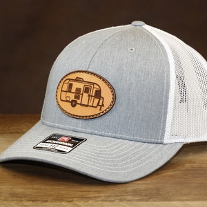 May include: A gray and white trucker hat with a brown leather patch featuring a vintage camper silhouette.
