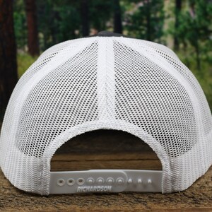 May include: White and black mesh trucker hat with an adjustable strap that says "RICHARDSON" on the back.