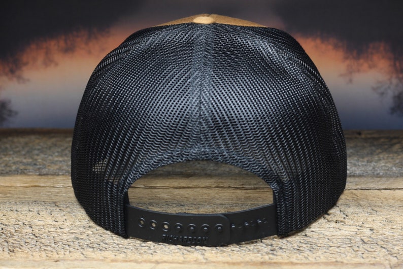 May include: A brown and black baseball cap with a black mesh back. The cap has a black adjustable strap with the word "Richardson" printed on it.