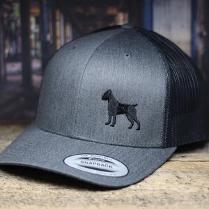 May include: A gray and black trucker hat with a black embroidered dog silhouette on the front. The hat has a black mesh back and a gray front panel. The hat is labeled "The Authentic Snapback" on the back.