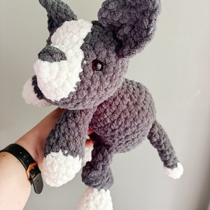 May include: A gray and white crocheted stuffed dog toy with black eyes. The dog is sitting up with its paws in the air.