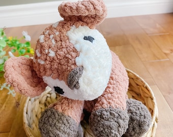 May include: A brown and white crocheted deer plush toy sitting in a woven basket. The deer has brown and white fur and black eyes.