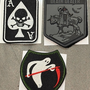 May include: Three embroidered patches: a rectangular black patch with a white ace of spades and skull design, a gray rectangular patch featuring a horse-mounted figure with the text DEATH DEALER, and a shield-shaped black patch with a white ghost holding a red scythe.