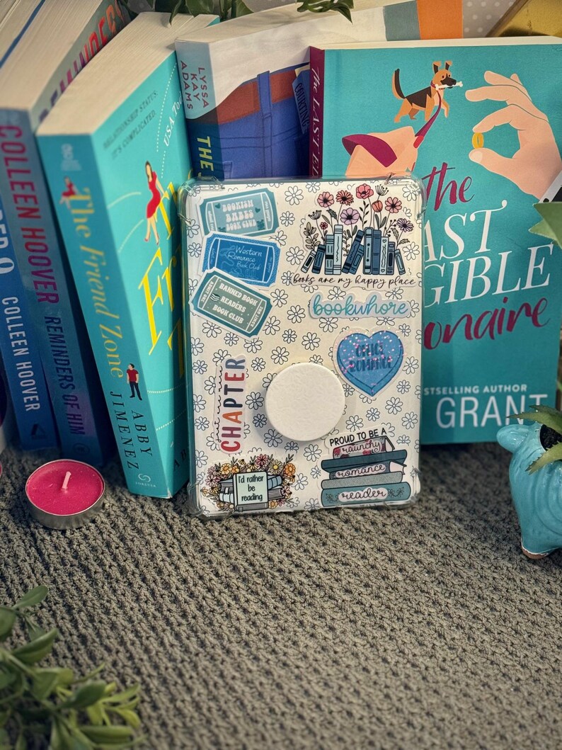 K&ouml;nnte beinhalten: Eine wei&szlig;e Handyh&uuml;lle mit Buchthema und bunten Aufklebern. Die Aufkleber zeigen B&uuml;cherstapel, Blumen und Text, der "B&uuml;cher sind mein gl&uuml;cklicher Ort" und "Bookwhore" sagt.