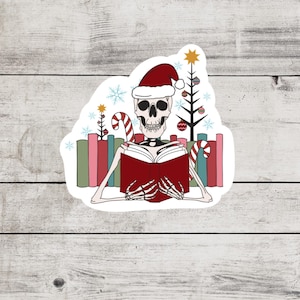 May include: A skeleton wearing a Santa hat is reading a book in front of a stack of colorful books and Christmas trees.