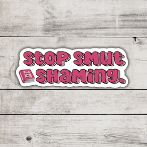 May include: A sticker with the text "STOP SMUT SHAMING" in pink bubble letters with a white outline. A small pink book with the words "ALL SPICE, NO PLOT" is in the lower left corner. The sticker is on a white wooden background.