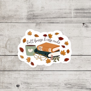 May include: A white sticker with a fall theme featuring a stack of books, a cup of coffee, and glasses. The text reads "fall breeze & cozy reads".