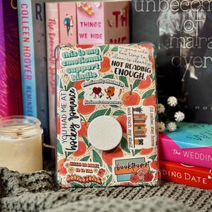 K&ouml;nnte beinhalten: Eine rosa und orangefarbene Handyh&uuml;lle mit verschiedenen Aufklebern. Die Aufkleber beinhalten "This is my emotional support kindle", "You had me at hockey romance", "Where in the heart do you go to the bookstore", "Booktrovert" und "Anyone who has time to clean is clearly not reading enough".