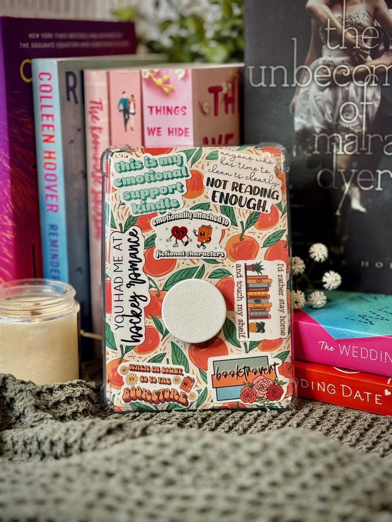 K&ouml;nnte beinhalten: Eine rosa und orangefarbene Handyh&uuml;lle mit verschiedenen Aufklebern. Die Aufkleber beinhalten "This is my emotional support kindle", "You had me at hockey romance", "Where in the heart do you go to the bookstore", "Booktrovert" und "Anyone who has time to clean is clearly not reading enough".