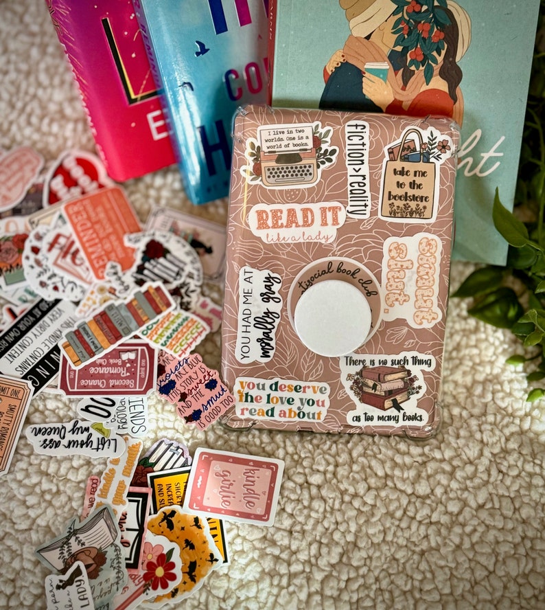 May include: A brown box with a variety of colorful stickers on it. The stickers feature book-related quotes and illustrations, including "Read it like a lady", "You had me at morally gray", "Take me to the bookstore", and "There is no such thing as too many books".
