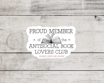 May include: White sticker with black text that reads "Proud Member of the Antisocial Book Lovers Club. Please Leave Me Alone."  A black and white illustration of an open book is above the text. Two small pink hearts are on either side of the text "of" and "the".