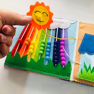 Puede incluir: Un libro de fieltro para ni&ntilde;os con un arco&iacute;ris, un sol, una casa y cuentas. Las cuentas se pueden mover a lo largo del arco&iacute;ris.