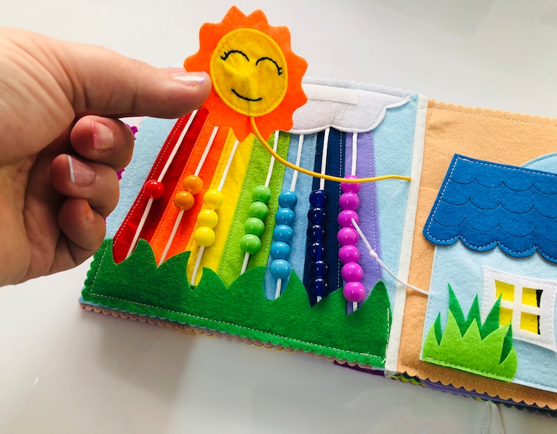 Puede incluir: Un libro de fieltro para ni&ntilde;os con un arco&iacute;ris, un sol, una casa y cuentas. Las cuentas se pueden mover a lo largo del arco&iacute;ris.