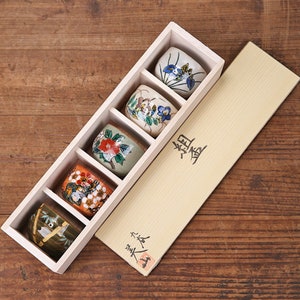 May include: A wooden box with a lid containing five small ceramic cups with floral designs. The box is labeled "翠香" in Japanese characters.
