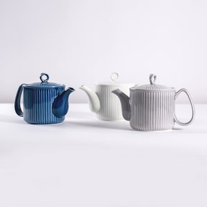 May include: Three ceramic teapots in different colors: blue, white, and gray. Each teapot has a ribbed design and a lid with a small knob.