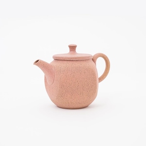 May include: A pink ceramic teapot with a textured surface and a lid. The teapot has a round body and a curved handle.