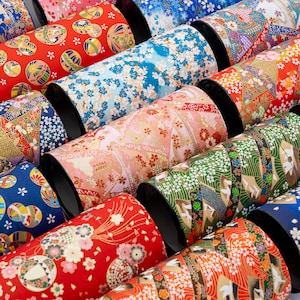 May include: A collection of cylindrical containers with black rims, wrapped in colorful Japanese paper. The paper features various patterns, including floral designs, geometric shapes, and traditional motifs in red, blue, and green.