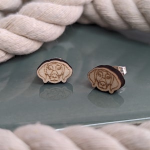 May include: A pair of wooden earrings featuring a laser-cut design of a dog's head. The earrings are brown and have silver posts.