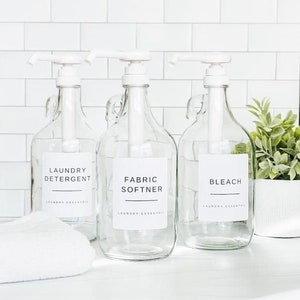 May include: Three clear glass bottles with white pump tops and labels. The labels read "Laundry Detergent", "Fabric Softner", and "Bleach".