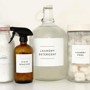 May include: Three clear glass bottles with white labels. The bottles contain laundry detergent, laundry pods, and stain remover. The labels have black text that reads "Laundry Detergent", "Laundry Pods", and "Stain Remover".