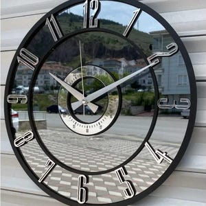 May include: A contemporary round wall clock with a black frame and a mirrored face. The clock has silver numerals and hands, with a smaller, mirrored inner clock face. The clock's design creates a layered, dimensional effect.