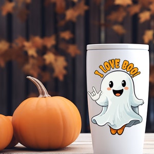 Op de afbeelding: Witte reistumbler met een cartoon-spook dat een wit laken en oranje schoenen draagt. Het spook heeft een vrolijk gezicht en steekt zijn hand omhoog in een rock-and-roll-gebaar. De tekst op de beker luidt "I Love Boo!"