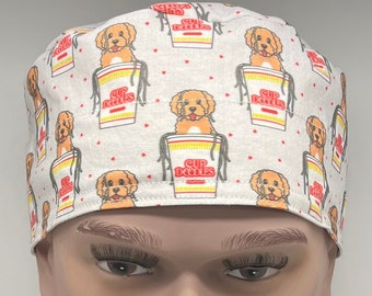 May include: White surgical scrub cap with a repeating pattern of a golden doodle dog in a cup of noodles. The words "Cup Doodles" are printed on the cup. Small red hearts are scattered across the background.