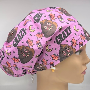 May include: A pink surgical scrub hat with a repeating pattern of brown poop emojis with fangs and wings, a crescent moon, and the text "Crazy" in black.