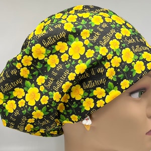 Puede incluir: Un gorro de quirófano negro con un estampado floral amarillo y el texto "Suck it up Buttercup" repetido en todo el gorro.