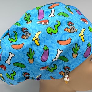 May include: A blue scrub hat with a colorful pattern of various foods, including bananas, eggplants, sausages, and cacti. The hat has a tie on the back.