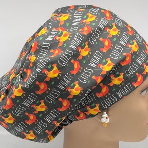 Puede incluir: Un gorro de quirófano negro con un patrón repetido de pollos amarillos y rojos y el texto "Guess What?" impreso en él.