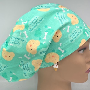 May include: A turquoise blue surgical scrub hat with a repeating pattern of yellow cartoon dogs, white bones, and the text "There is a fracture. We need to fix it."