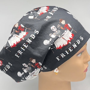 Puede incluir: Un gorro de quirófano negro con un estampado de personajes de películas de terror tomando el té. El texto "FRIENDS" se repite en el gorro.