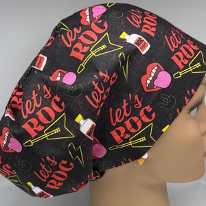 Może przedstawiać: Czarny czepek chirurgiczny z motywem rock and rolla. Czepek zawiera czerwony napis "let's ROC", a także gitary elektryczne, usta, błyskawice i butelki. Wzór jest nadrukowany na czarnym tle.