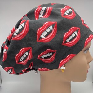 May include: Black scrub hat with a repeating pattern of red lips with white fangs.