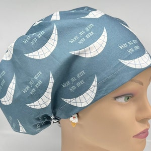 May include: A blue scrub hat with a white pattern of a Cheshire Cat grin and the text "We're all quite mad here" repeated.