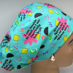 May include: A light blue surgical scrub cap with a repeating pattern of geometric shapes and the text "I am unable to quit as I am currently too legit." The cap is made of a soft fabric and is designed to cover the hair during medical procedures.