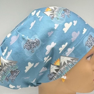 May include: A light blue surgical scrub cap with a repeating pattern of white clouds and mountain graphics. The cap has the words "Plastic Surgery" and "Mountains & Hills" printed on it.