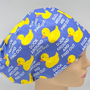 May include: Blue surgical scrub hat with a repeating pattern of yellow rubber ducks and the text "Duck Around and Find Out".