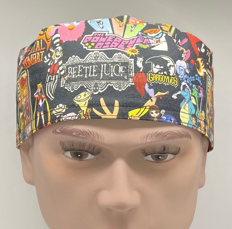 May include: A black scrub hat with a colorful cartoon print featuring characters from popular shows like "The Powerpuff Girls", "Beetlejuice", "Gargoyles", and "Dragon Tales".