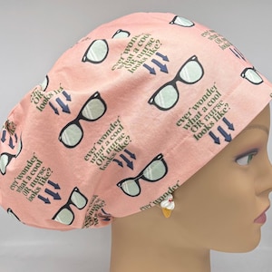 May include: A peach-colored surgical scrub cap with a repeating pattern of eyeglasses and the text "ever wonder what a cool OR nurse looks like?" in black. The cap is designed for medical professionals.