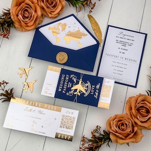 May include: A navy blue wedding invitation set featuring a passport-style booklet with gold foil airplane accents, a boarding pass with a QR code, a program card, and an envelope with a gold world map liner and a wax seal, accented by orange roses.