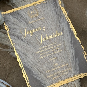 Peut inclure: Invitation de mariage à bordure dorée avec un fond texturé. L'invitation indique "Jaguar & Johmisha" et comprend la date, l'heure et le lieu du mariage.
